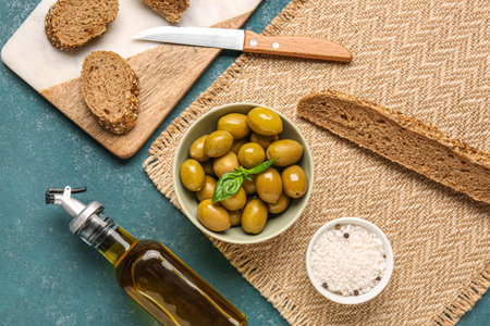 Bowl with ripe olives, bread and bottle of oil on green backgroundの写真素材