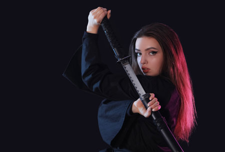 Beautiful young woman with katana on black backgroundの写真素材