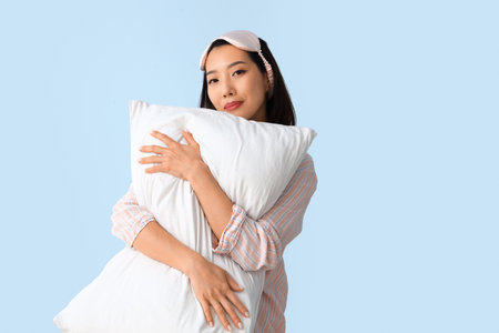 Beautiful Asian woman in pajamas with pillow on blue backgroundの写真素材