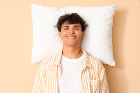 Young man with pillow on beige backgroundの写真素材