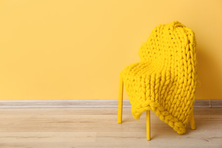 New knitted blanket on chair near yellow wall in roomの写真素材