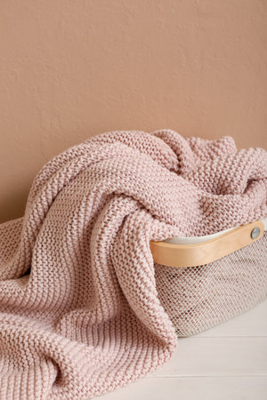 Basket with new soft blanket on table near beige wallの写真素材