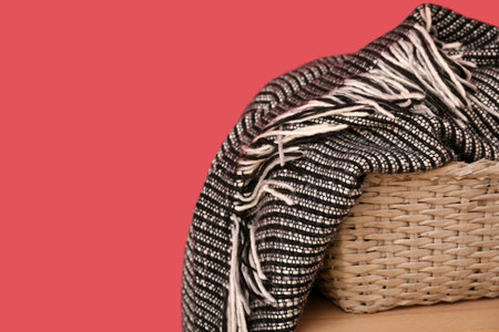Basket with new soft blanket on table near burgundy wall, closeupの写真素材