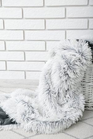 Basket with new soft blanket near light brick wall in room