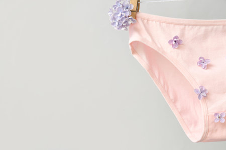 Stylish female panties with beautiful lilac flowers hanging on rope against white background,...