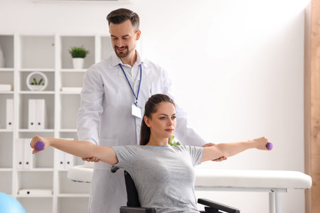 Male physiotherapist working with young woman in wheelchair at rehabilitation centerの写真素材