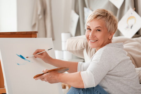 Mature female artist painting picture in workshopの写真素材