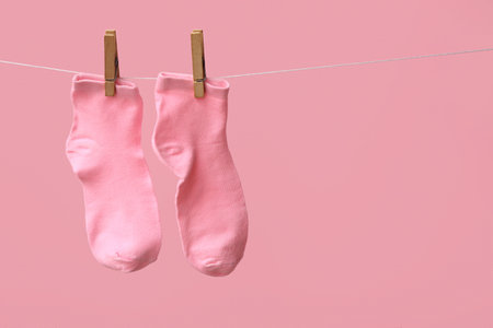 Pair of cotton socks hanging on rope against pink backgroundの写真素材