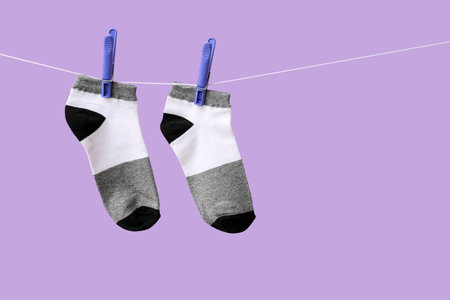 Pair of cotton socks hanging on rope against lilac backgroundの写真素材