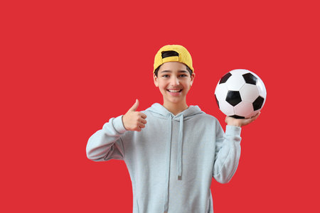 Little boy with soccer ball showing thumb-up on red backgroundの写真素材
