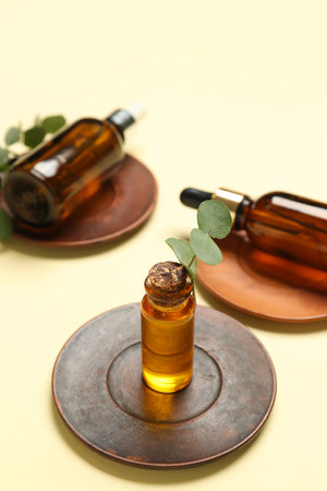 Wooden plates with bottles of cosmetic oil and eucalyptus branch on pale yellow backgroundの写真素材