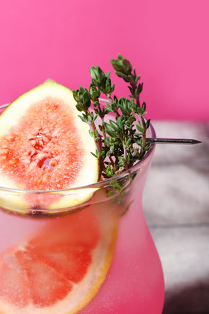 Fresh summer cocktail with fig, grapefruit and thyme near pink wallの写真素材