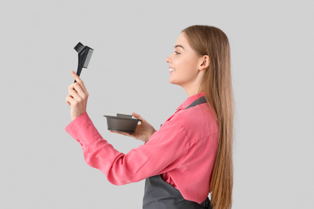 Female hairdresser with bowl and brush for hair dye on gray backgroundの写真素材