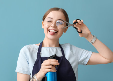 Female hairdresser with scissors and spray showing tongue on blue background, closeupの写真素材