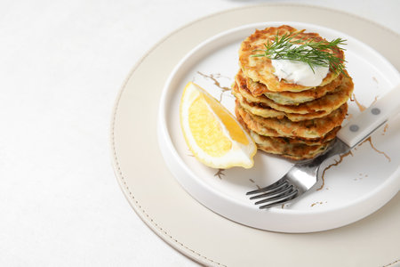 Plate of tasty zucchini fritters with sour cream on light backgroundの写真素材