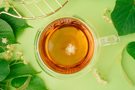 Glass cup of linden tea on green background