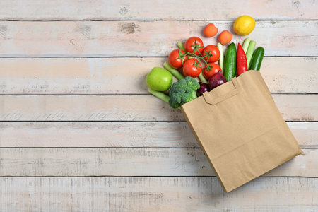 Paper bag with fresh vegetables and fruits on light wooden backgroundの写真素材