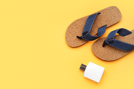 Flip-flops with bottle of sunscreen cream on orange backgroundの写真素材