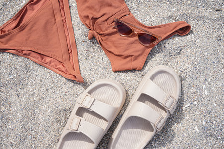 Beige flip-flops with swimsuit and sunglasses on sandy beach backgroundの写真素材