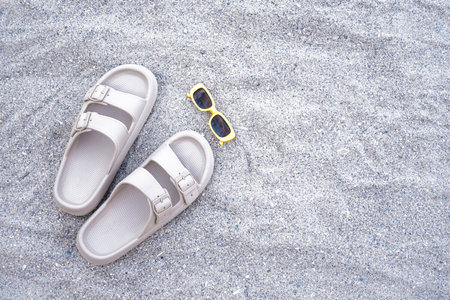 Beige flip-flops with sunglasses on sandy beach backgroundの写真素材