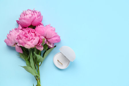 Box with beautiful ring and peony flowers on color backgroundの写真素材
