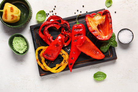 Wooden board with tasty grilled peppers on light backgroundの写真素材