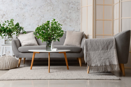 Interior of living room with cozy gray sofa and blooming jasmine flowers on coffee table