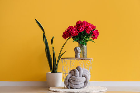 Vase of red peonies with figurine and houseplant near yellow wallの写真素材
