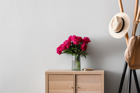 Vase of red peonies with coat rack and dresser near light wallの写真素材