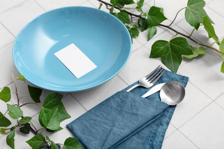Beautiful table setting with plant branches and blank invitation card on white tiled tableの写真素材