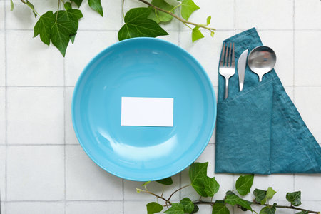 Beautiful table setting with plant branches and blank invitation card on white tiled tableの写真素材