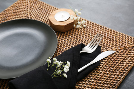 Beautiful table setting with clean plate, gypsophila flowers, place mat and candle on black tableの写真素材