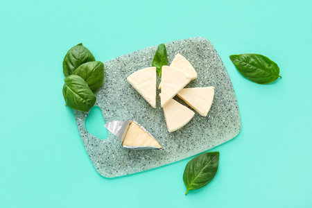 Board with triangles of tasty processed cheese and basil leaves on turquoise backgroundの写真素材
