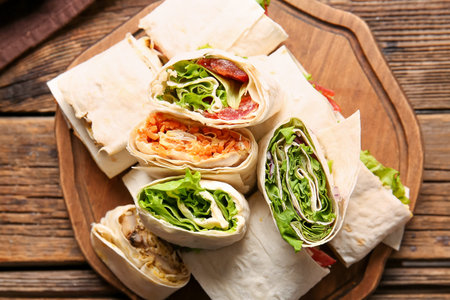 Board of tasty lavash rolls with vegetables and greens on wooden backgroundの写真素材