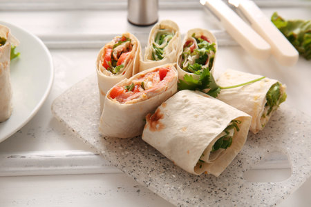 Board of tasty lavash rolls with vegetables on white wooden background