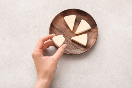 Woman eating triangle of tasty processed cheese on light backgroundの写真素材