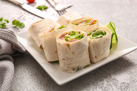 Plate of tasty lavash rolls with vegetables on gray background