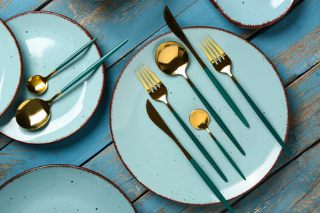 Clean plates with set of golden cutlery on blue wooden tableの写真素材