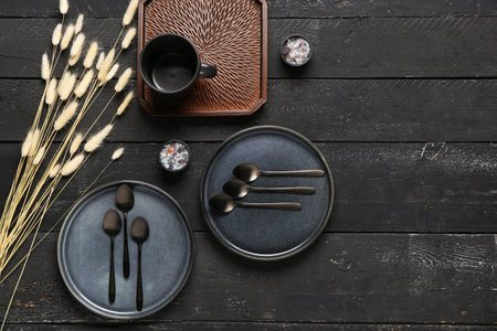 Clean plates with set of spoons and dried lagurus on black wooden tableの写真素材