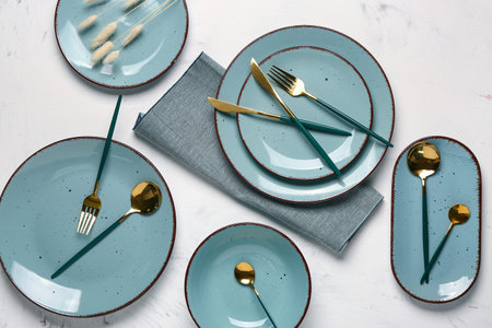 Table setting with clean plates, golden cutlery and napkin on white background