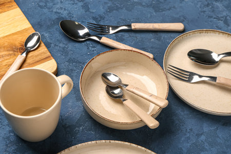 Clean plates, bowl, cup and cutlery on blue tableの写真素材