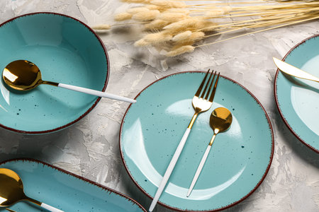 Clean plates with golden cutlery and dried lagurus on gray grunge tableの写真素材