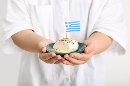 Woman holding plate with mozzarella cheese and flag of Greece on white background