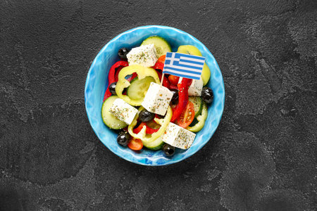 Bowl of salad with feta cheese, olives and Greek flag on black grunge tableの写真素材