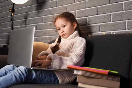 Little girl with laptop doing lessons at home late in the evening