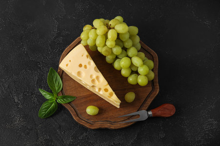 Wooden board with tasty Swiss cheese and grapes on black backgroundの写真素材