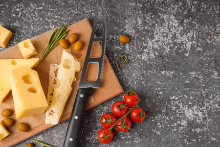 Board with pieces of Swiss cheese and olives on gray background