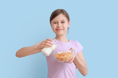 Little girl with milk and cornflakes on light blue backgroundの写真素材