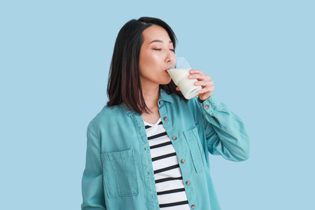 Beautiful Asian woman drinking milk on light blue backgroundの写真素材