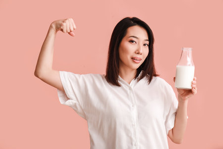 Strong Asian woman with bottle of milk on pink backgroundの写真素材